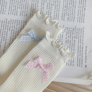 Close-up of white ribbed knit socks with ruffled trim and pastel bow tie details