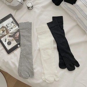 Flat lay of ribbed two-toe Tabi socks in grey, beige, and black on a cozy white bed