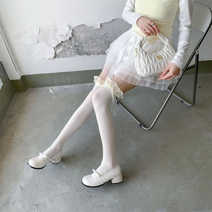 Detail of white over-knee socks with lace trim, bow accents, and Mary Jane shoes