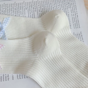 Detail of white ribbed cotton socks with light blue and pink bow tie accessories