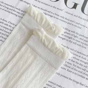 Close-up of white knit ruffle socks with diamond texture on a vintage magazine