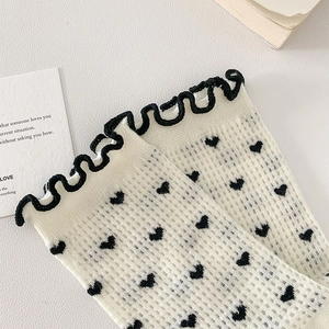 Detail of white mesh socks featuring black heart prints and ruffled lettuce edge trim