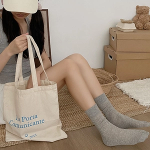 Detail view of grey ribbed mid-calf split toe socks paired with a beige canvas tote bag
