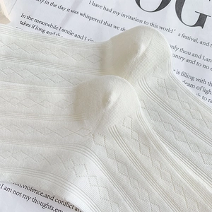 Detailed close-up of white mesh knit socks with diamond patterns and ruffled lace edges