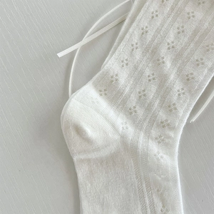 Dettaglio della trama traforata in pizzo bianco con decorazione a fiocco in nastro