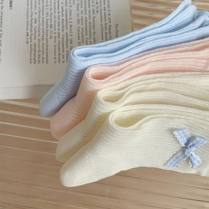 Detail of knit rib socks featuring cute blue plaid bow accents on pastel cotton fabric