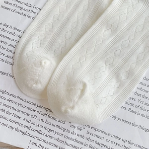 Close-up of white mesh knit socks with diamond pattern on vintage poem paper
