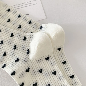 Close-up of cream mesh knit socks with black heart pattern and breathable texture