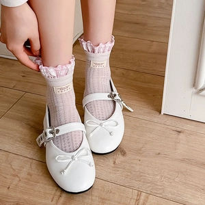White Mary Jane shoes with lace socks and bow detail on a wooden floor