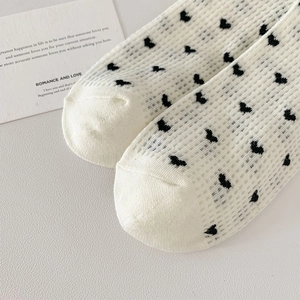 Close-up of white mesh socks with black heart patterns and breathable knit texture
