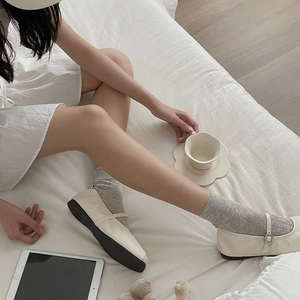 Detail of off-white Mary Jane flats worn with gray jacquard mesh socks in a home setting