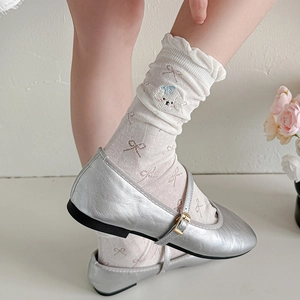 Detail of cream ruffle socks with bow patterns and dog embroidery worn with silver shoes