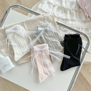 Dettaglio di calze a rete velate con nastri di pizzo nei colori bianco, rosa, grigio e nero