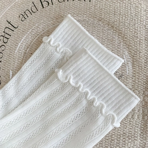 Detail of white mesh socks with ruffled edges on a glass plate with woven texture