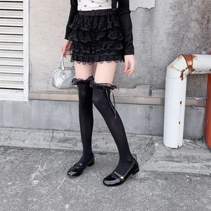 Close-up of black over-knee socks with lace ruffles and ribbon bows in gothic lolita style