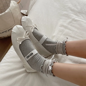 White ballet flats with bow straps and grey frill trim socks on soft bedding