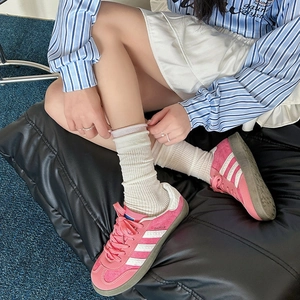 Dettaglio di sneaker in pelle scamosciata rosa con strisce bianche e calze crema