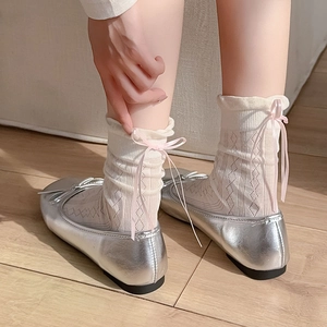Dettaglio calzini in pizzo bianco con fiocchi rosa e ballerine argento su pavimento in legno
