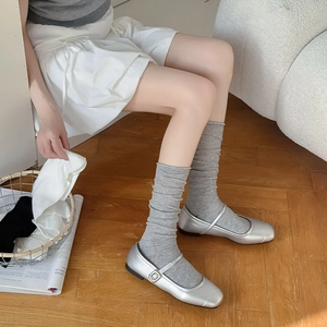 Detail of light grey cotton knit slouch socks with silver Mary Jane shoes on wood floor