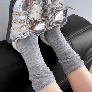 Close-up of grey ribbed knit slouch socks styled with silver sneakers on black leather