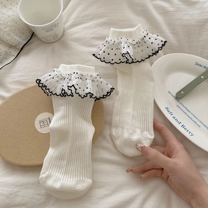 Détail de chaussettes blanches côtelées avec volants en dentelle mesh à pois noirs