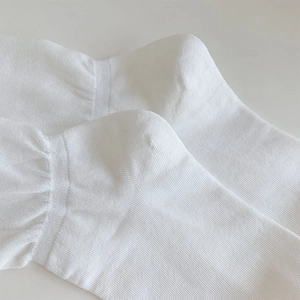 Macro detail of breathable white ribbed knit fabric on a thin minimalist calf sock