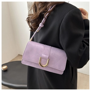 Detail view of purple matte shoulder bag with gold U-shaped lock on black blazer outfit