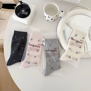Détail de quatre paires de chaussettes à fleurs brodées en noir, rose, gris et blanc crème
