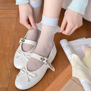 Close-up of white Mary Jane shoes with heart patterned mesh socks on wooden floor