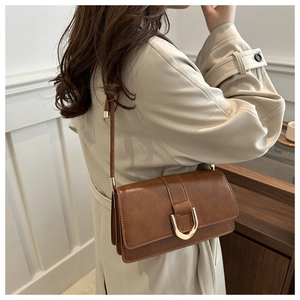 Detailed close-up of brown leather crossbody bag with gold U-shaped magnetic buckle