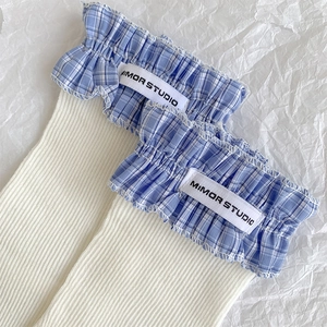 Detailed view of white ribbed socks featuring blue plaid lace trim and a logo label