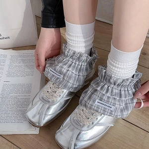 Close-up of silver metallic sneakers featuring grey plaid ruffled trim and ribbon details