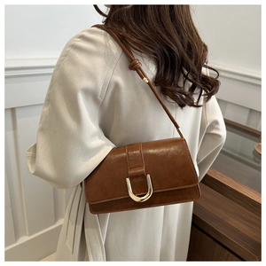 Brown glossy leather underarm bag with gold U-shaped buckle worn with a beige trench coat