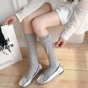 Close-up of grey calf socks with white ribbon bow and silver leather ballet flats