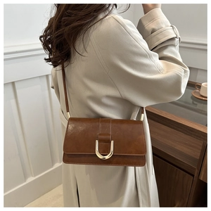 Brown vintage flap bag with gold U-shaped buckle styled over a woman's shoulder
