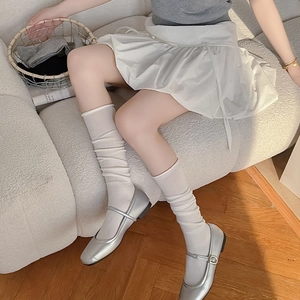 Detail of white cotton slouch socks paired with silver Mary Jane flat shoes on a sofa