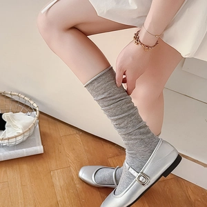 Close-up of grey cotton slouch socks paired with silver metallic Mary Jane flat shoes