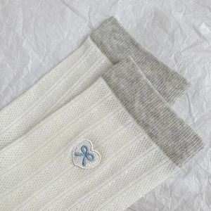 Detail of white ribbed crew socks with blue bow heart embroidery and grey contrast cuffs