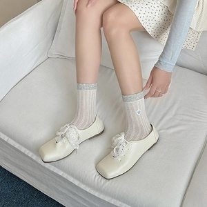 Close-up of bow embroidery on mesh socks paired with lace flat shoes in cream