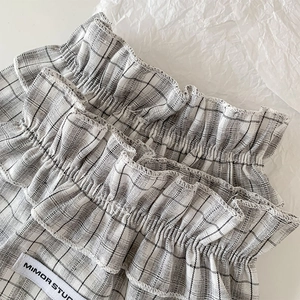 Detail of grey plaid leg warmer featuring ruffled edges and a stitched brand label