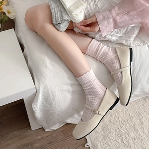 Close-up of beige Mary Jane flats with ankle straps worn with pink striped mesh socks