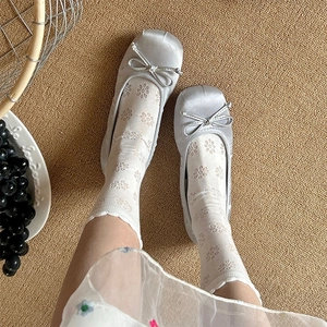 Close-up of light grey satin ballet flats with silver bows and white lace socks on a mat
