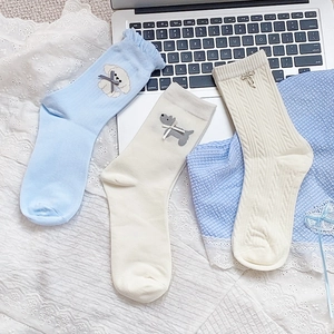 Detailed view of three pastel socks with cute dog embroidery and bow accents in a cozy setting