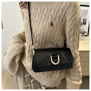Close-up of black leather crossbody bag featuring a golden U-shaped metallic clasp detail