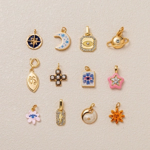 Macro shot of twelve assorted stainless steel charms featuring enamel, pearls, and moon motifs
