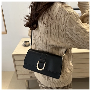 Detail view of black matte underarm bag with gold horseshoe buckle on beige sweater