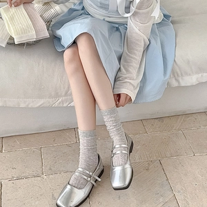 Detail of grey lace floral textured socks paired with silver metallic Mary Jane shoes