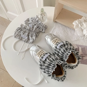 Detailed top view of plaid lace leg warmers styled with metallic sneakers on a white table