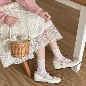 Detail of white mesh socks with lace trim paired with beige Mary Jane shoes and skirt