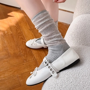 Close-up of white Mary Jane flats with bow detail and grey striped slouch socks